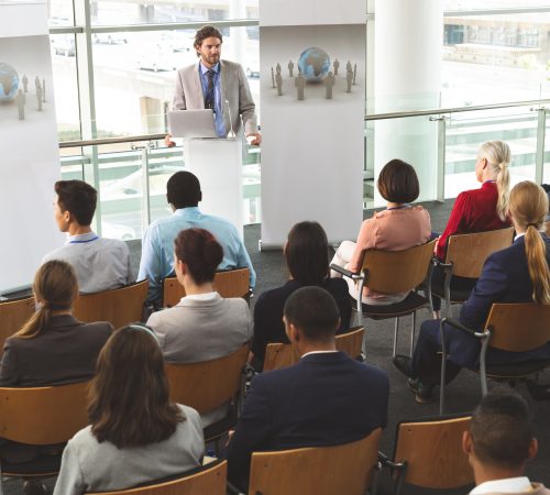 High angle view of Caucasian male speaker with laptop having a presentation in front of business people sitting at business seminar in office building